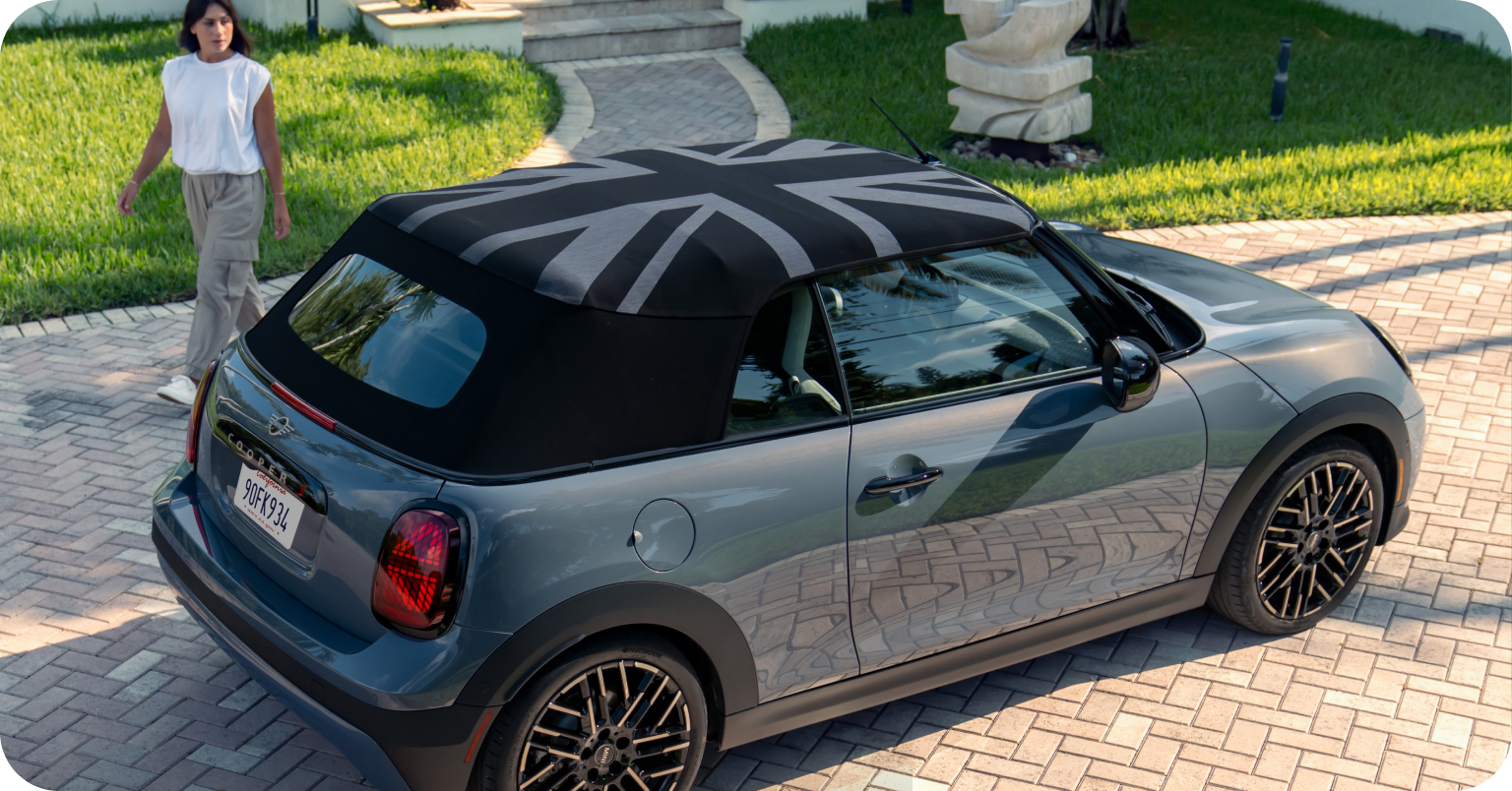 Woman standing behind the side view of grey MINI Cooper Convertible on a suburban street.