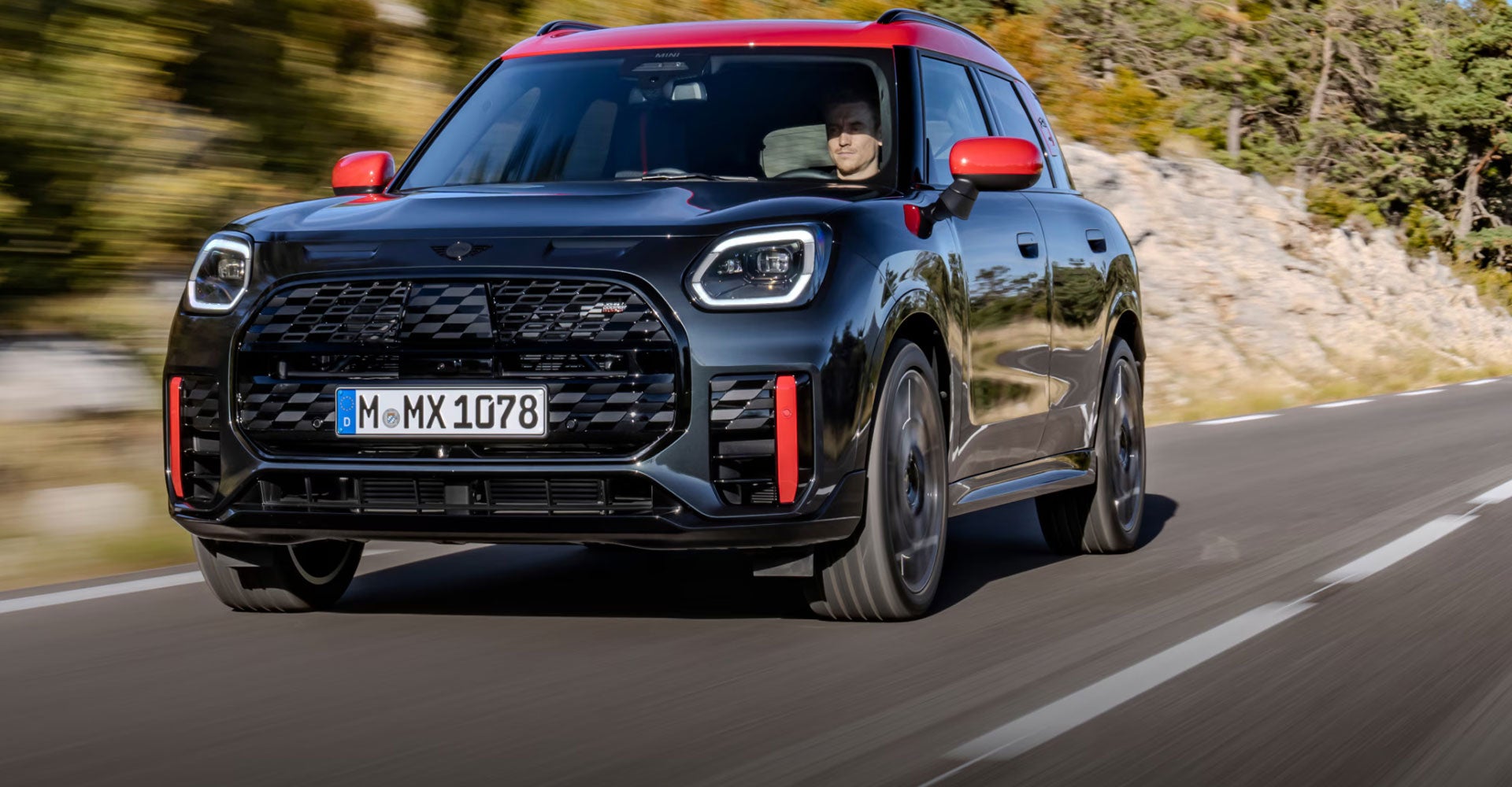 Front view of a MINI JCW Countryman ALL4 driving on a road with a blurred background.