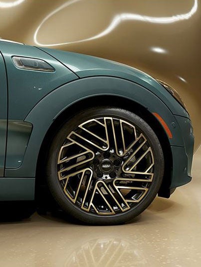 Closeup of the exclusive 18” Untold spoke 2-tone wheels on a MINI Clubman Untold Edition, which has a giant CGI, inflating, shiny, brass balloon coming from the side of the car.